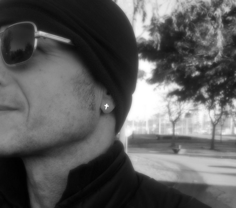 May include: A black and white photo of a person wearing a black beanie and sunglasses. The person is wearing a small cross earring.