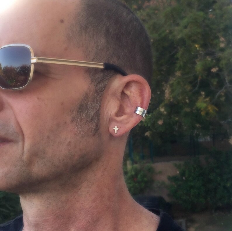 May include: A man wearing a pair of sunglasses with a gold cross earring in his left ear and a silver ear cuff in his right ear.