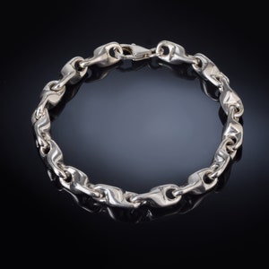 K&ouml;nnte beinhalten: Ein silbernes Kettenarmband mit einem einzigartigen Gliederdesign. Das Armband ist aus poliertem Silber gefertigt und hat einen sicheren Verschluss.