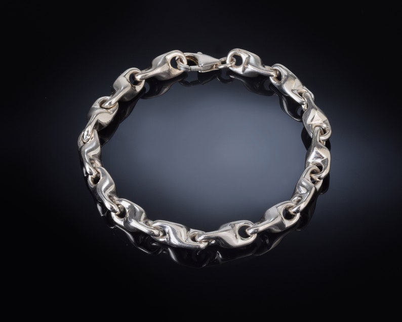 K&ouml;nnte beinhalten: Ein silbernes Kettenarmband mit einem einzigartigen Gliederdesign. Das Armband ist aus poliertem Silber gefertigt und hat einen sicheren Verschluss.