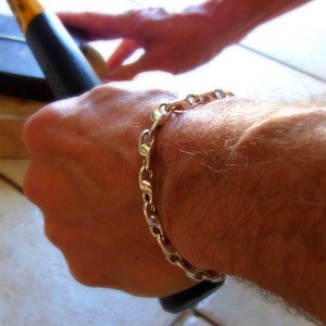 K&ouml;nnte beinhalten: Ein silbernes Kettenarmband mit einem Curb-Link-Design. Das Armband wird am Handgelenk getragen.