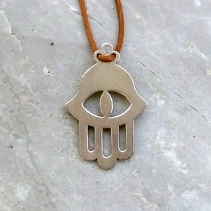 May include: A silver hamsa hand charm necklace with a brown suede cord. The hamsa hand is a symbol of protection and good luck.