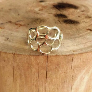May include: A silver ring with a unique, openwork design featuring a series of interconnected circles. The ring is displayed on a wooden surface.