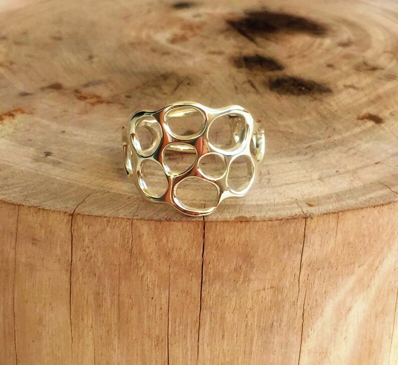 May include: A silver ring with a unique, openwork design featuring a series of interconnected circles. The ring is displayed on a wooden surface.