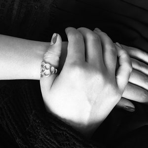 May include: A close-up of two hands clasped together. The hand on top is wearing a silver ring with a honeycomb design.