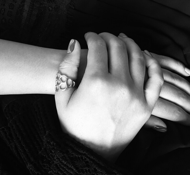 May include: A close-up of two hands clasped together. The hand on top is wearing a silver ring with a honeycomb design.