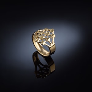 May include: A gold ring featuring a geometric, openwork design. The ring is crafted from a single piece of metal and has a smooth, polished finish.
