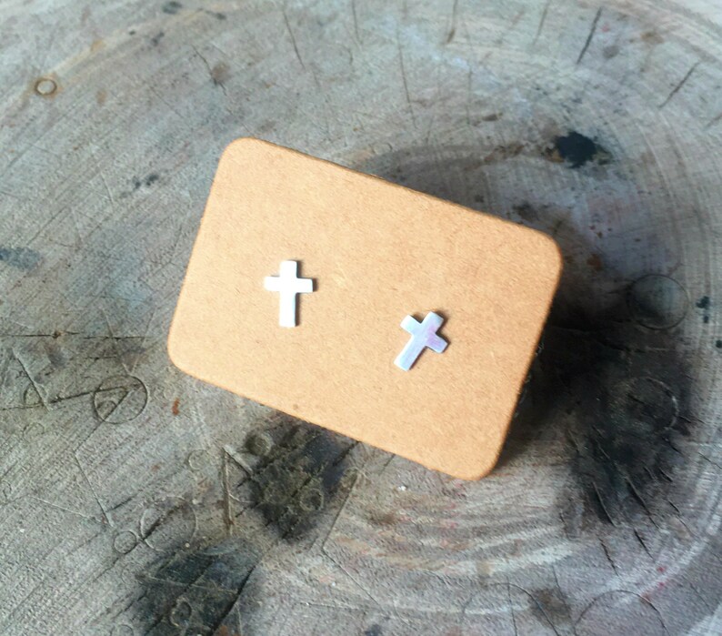 May include: A pair of silver cross stud earrings on a brown card.