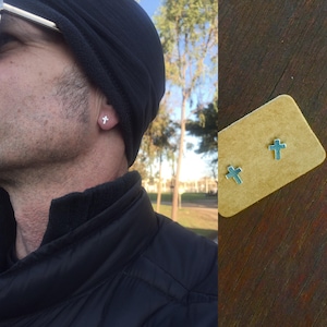 May include: A pair of silver cross stud earrings. The earrings are shown on a person's ear and on a small brown card.