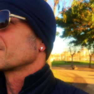 May include: A man wearing a blue beanie and sunglasses with a small cross earring in his left ear.