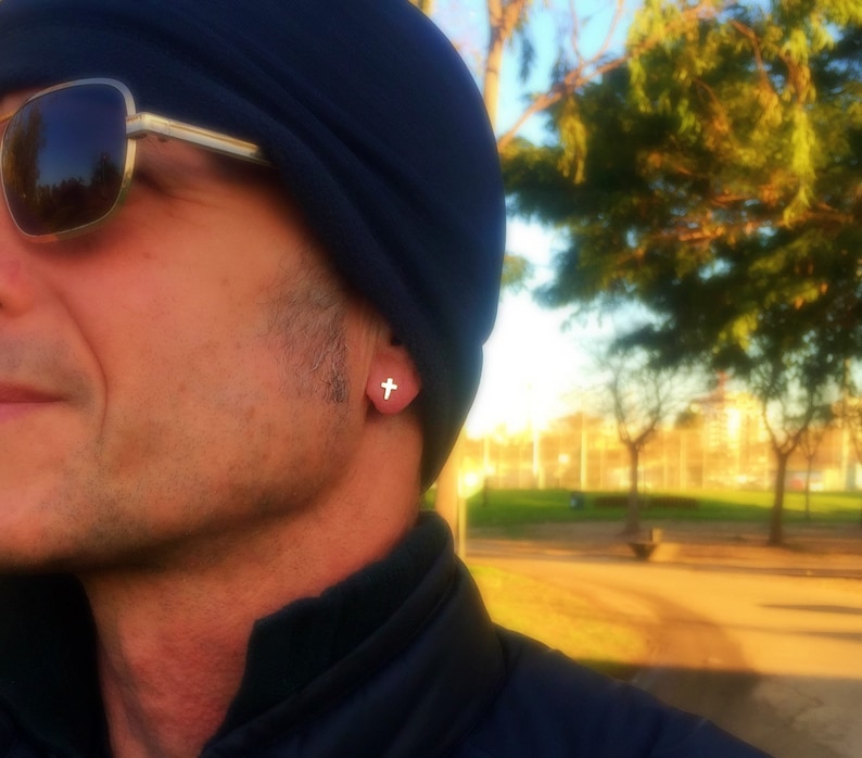 May include: A man wearing a blue beanie and sunglasses with a small cross earring in his left ear.