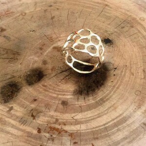 May include: A gold-toned ring with a geometric, openwork design. The ring is made of metal and has a honeycomb-like pattern.
