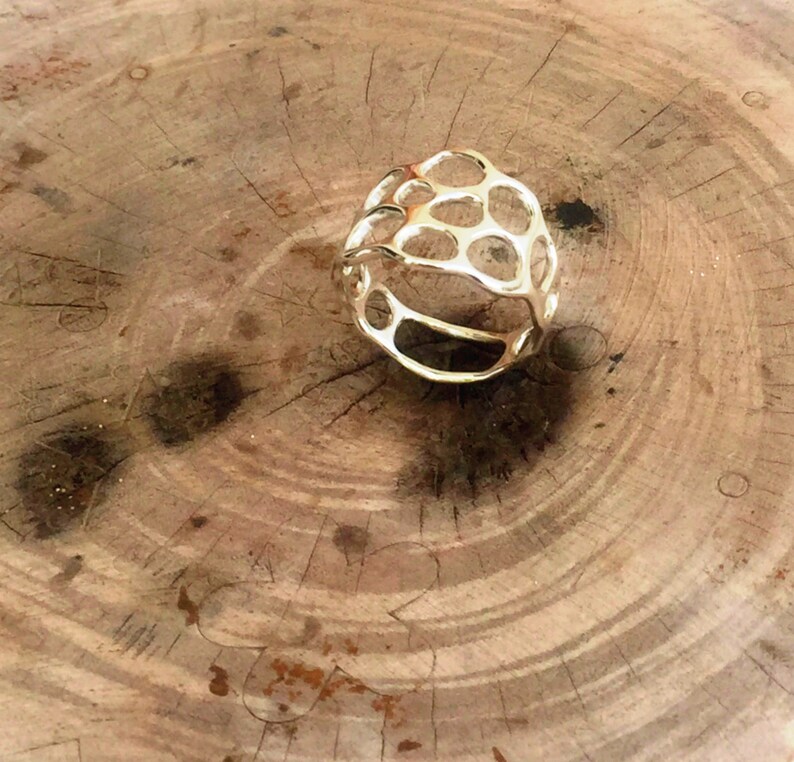 May include: A gold-toned ring with a geometric, openwork design. The ring is made of metal and has a honeycomb-like pattern.