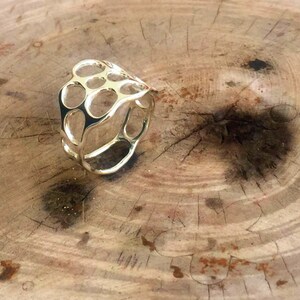 May include: A gold ring with a unique, openwork design. The ring is made of a series of interconnected circles and ovals, creating a delicate and intricate pattern.