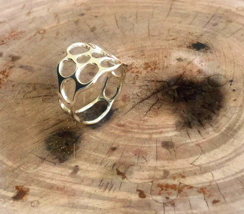 May include: A gold ring with a unique, openwork design. The ring is made of a series of interconnected circles and ovals, creating a delicate and intricate pattern.