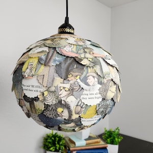 May include: A spherical lampshade made from pages of a children's book featuring illustrations of a wolf and a monster. The lampshade is hanging from a black cord and a black ceiling fixture.