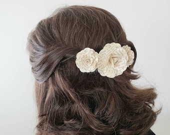 May include: Three paper flowers made from book pages, in a light cream color, are worn in a person's hair.