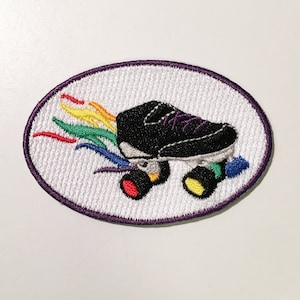 May include: Embroidered patch featuring a black roller skate with purple laces and colorful rainbow accents. The patch is oval-shaped with a white background and a purple border. The wheels are red, yellow, and blue.