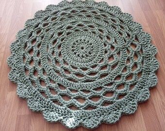 May include: A large, round, crocheted rug in a sage green colour. The rug has a circular pattern with multiple layers of crocheted stitches.
