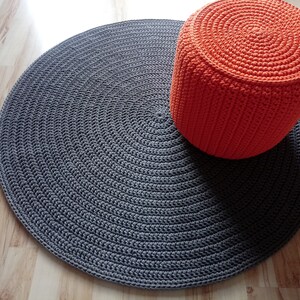 May include: A round grey crocheted rug with a bright orange crocheted pouffe on top.