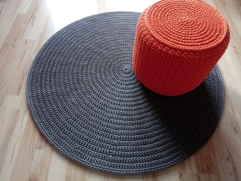 May include: A round grey crocheted rug with a bright orange crocheted pouffe on top.