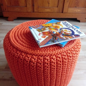 May include: Orange crocheted footstool with two children's books on top. The book on top is titled "Malowanie Neszele".