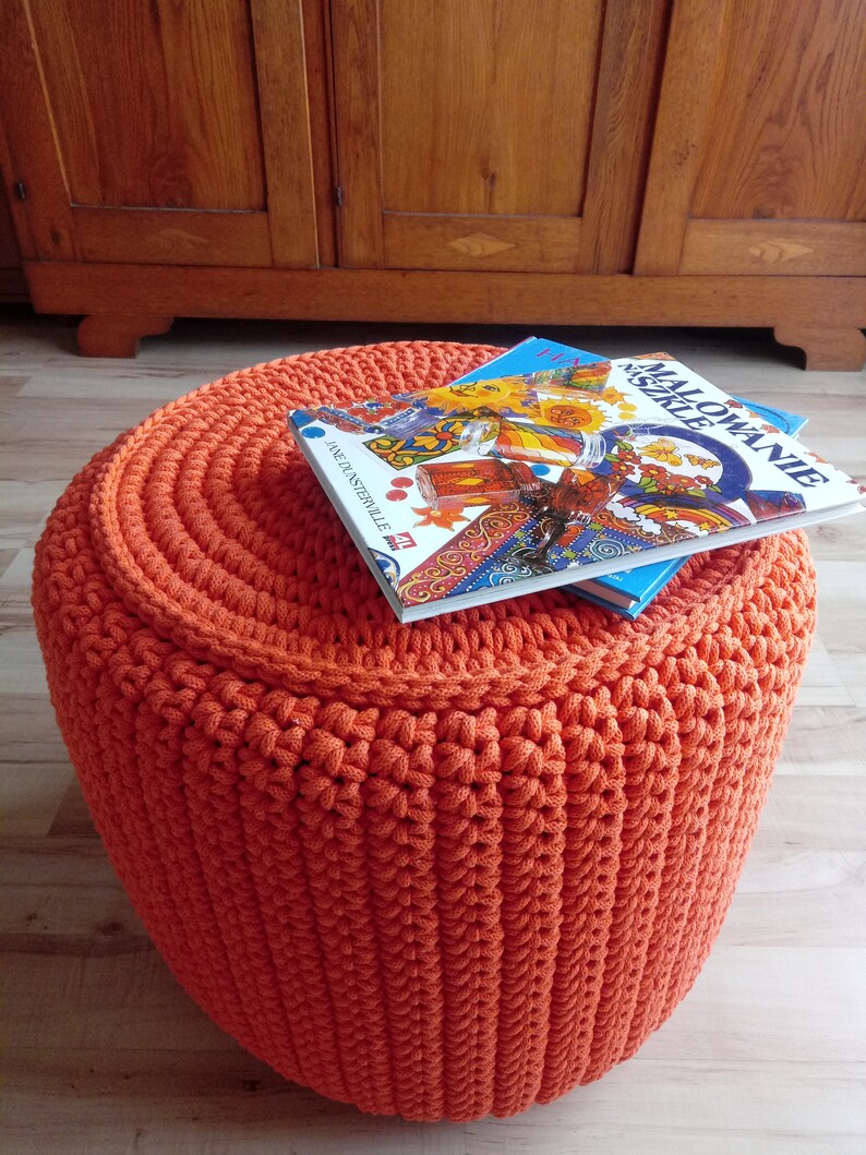 May include: Orange crocheted footstool with two children's books on top. The book on top is titled "Malowanie Neszele".