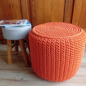May include: A bright orange crocheted footstool with a round top and a textured surface.