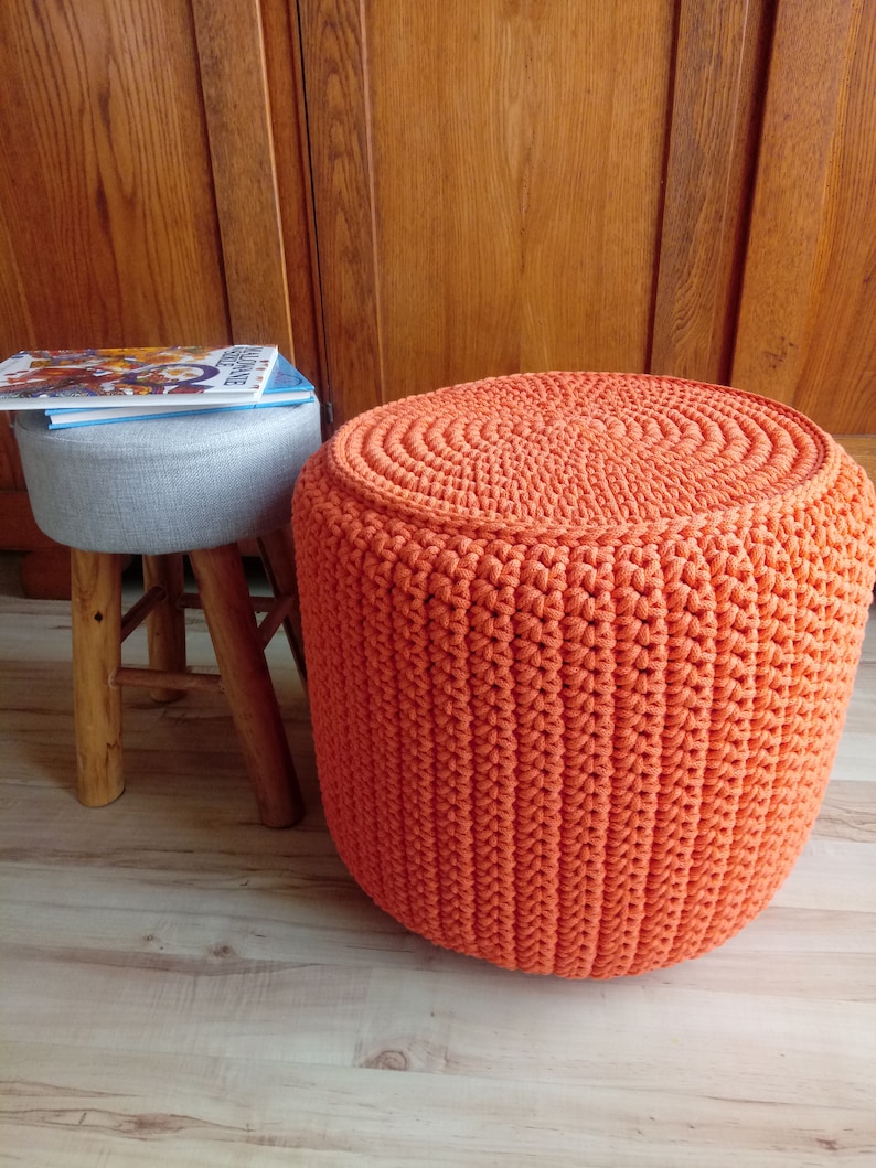 May include: A bright orange crocheted footstool with a round top and a textured surface.
