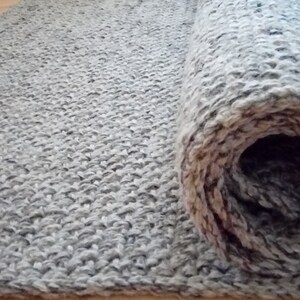 Könnte beinhalten: Ein grauer und weißer gewebter Teppich, der aufgerollt ist und die Textur des Materials zeigt.
