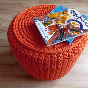 May include: Orange crocheted footstool with two books on top. The top book has a colourful cover with the title "Malowanie Szkiele" and the bottom book has a blue cover.