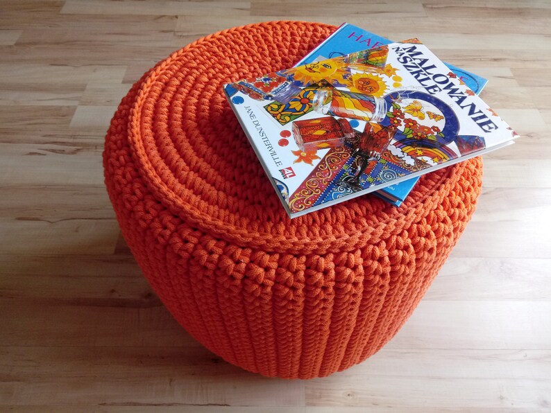 May include: Orange crocheted footstool with two books on top. The top book has a colourful cover with the title "Malowanie Szkiele" and the bottom book has a blue cover.