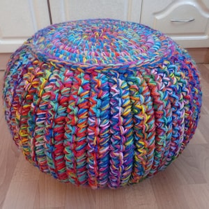 May include: A colourful crocheted footstool with a round shape and a multi-coloured yarn design.