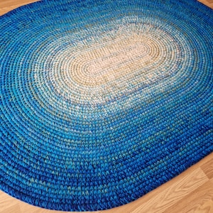 May include: An oval braided rug in blue and white with a gradient pattern. The rug is made from thick, woven rope and has a soft, textured surface.