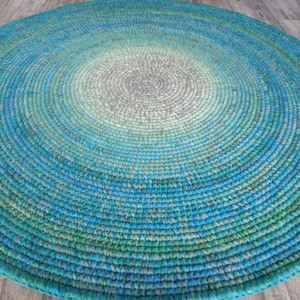 May include: A round, crocheted rug with a gradient of colors from light gray in the center to teal blue on the outer edge.