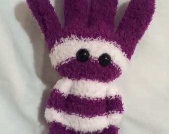 May include: A handmade plush toy shaped like a hand with five fingers and two feet. The toy is purple with white stripes and has two black button eyes. The plush is made of a soft, fuzzy material.