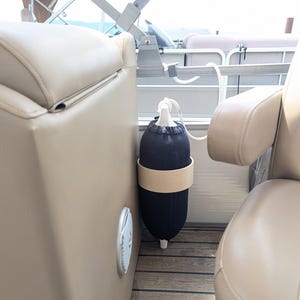 May include: A black boat fender with a beige band is secured to a boat. The fender is hanging next to a beige boat seat. The boat has a brown and beige wooden floor.