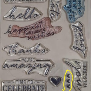 May include: A clear photopolymer stamp set featuring various sentiments including HUGE CONGRATS, hello, happiest birthday wishes, thanks, YOU'RE amazing, TIME TO CELEBRATE, just a note, You're in my thoughts, YOU ARE SO loved, and HERE'S TO you, plus a heart.