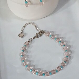 May include: A jewelry set featuring a bracelet and earrings. The bracelet and earrings are made with pink, faceted beads and small turquoise beads. The earrings hang from silver-colored hooks. The bracelet has a silver-colored chain and clasp.