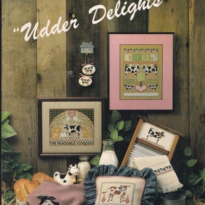 May include: A collection of cow-themed cross-stitch samplers and decorative items. The image features framed artwork, a pillow, a towel, and ornaments, all with cow motifs. The background is rustic wood, and the text "Udder Delights" is visible.