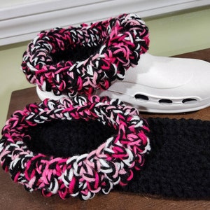 May include: White clogs with a black and pink crocheted boot cuff. The cuff is made with a thick yarn and has a fluffy texture.