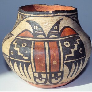 Op de afbeelding: Een traditionele Native American aardewerken pot met een geometrisch ontwerp in zwart, wit en rood. De pot heeft een gestileerd vogelontwerp met een centrale rode streep.