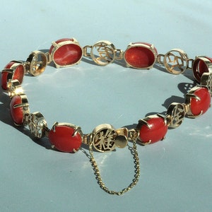 May include: A gold bracelet with red oval-shaped stones and Chinese characters. The bracelet has a clasp with a small chain.