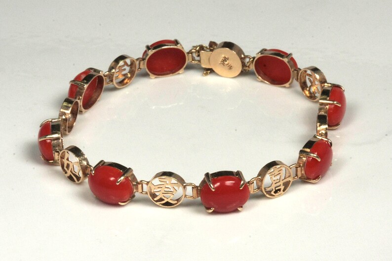 May include: A gold bracelet with red coral stones and Chinese characters. The bracelet has a clasp with the number "14K" on it.