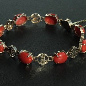 May include: A red coral bracelet with gold accents and a chain clasp. The bracelet features Chinese characters on the gold accents.