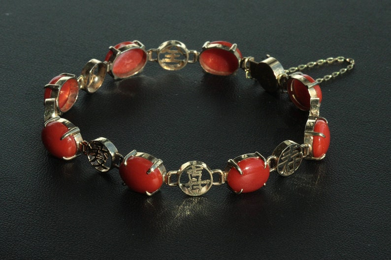 May include: A red coral bracelet with gold accents and a chain clasp. The bracelet features Chinese characters on the gold accents.