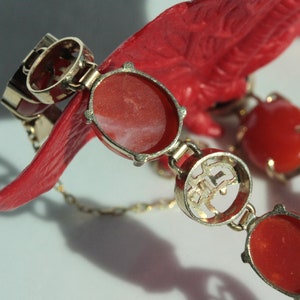 May include: A gold bracelet with red coral stones and Chinese characters. The bracelet has a clasp and is made of a delicate chain.