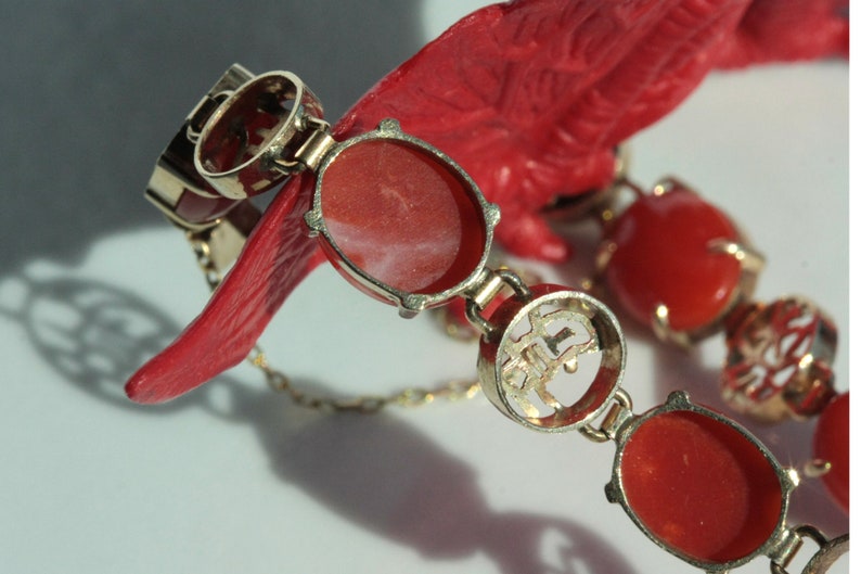 May include: A gold bracelet with red coral stones and Chinese characters. The bracelet has a clasp and is made of a delicate chain.
