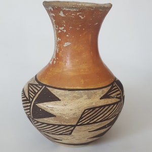 Puede incluir: Un pequeño jarrón de cerámica pintado a mano con un diseño geométrico en blanco y negro sobre un fondo marrón. El jarrón tiene un cuello estrecho y un cuerpo redondeado.