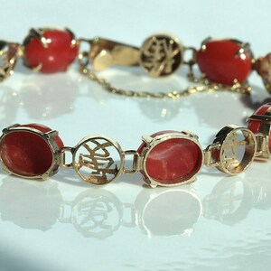 May include: A gold bracelet with red coral stones and Chinese characters. The bracelet is made of 14k gold and features a delicate chain.